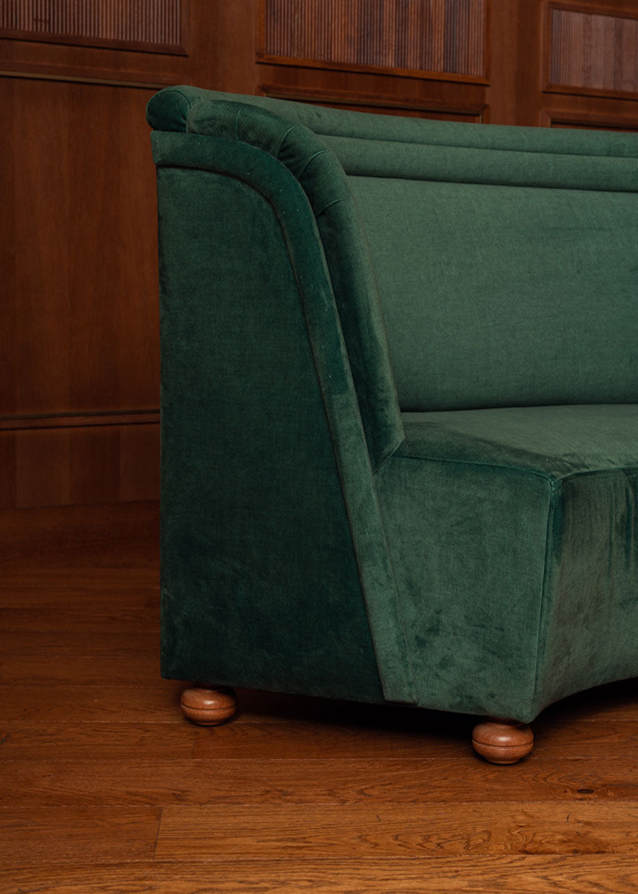 Banco curvado tapizado en terciopelo verde con patas de madera de haya.