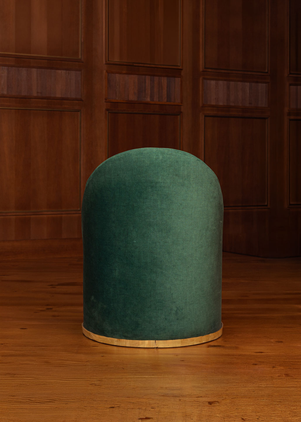 Butaca tapizada en terciopelo verde con zócalo dorado en la base.