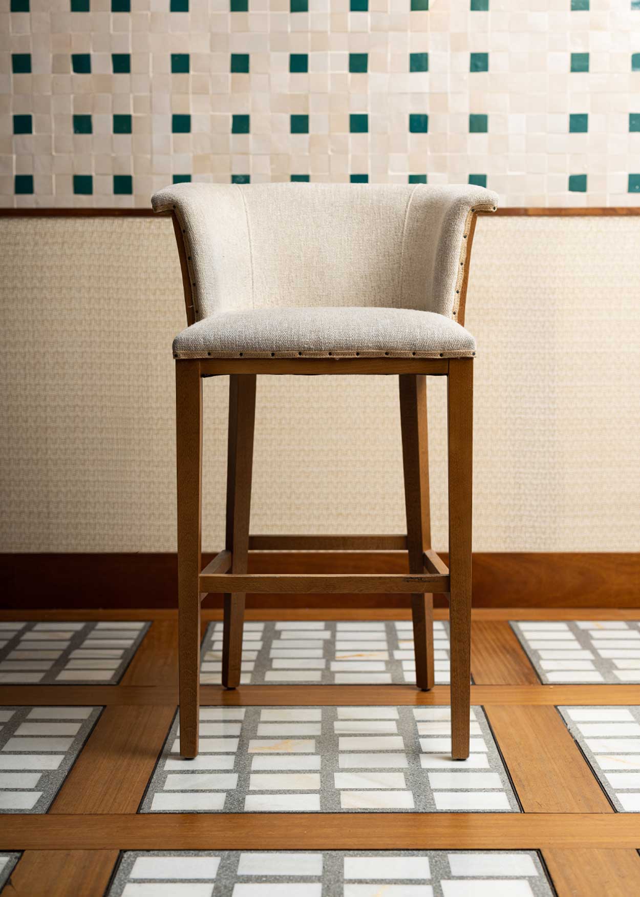 Taburete con estructura de madera de haya, tapizado en tela beige y acabado con un ribete de yute con remaches.