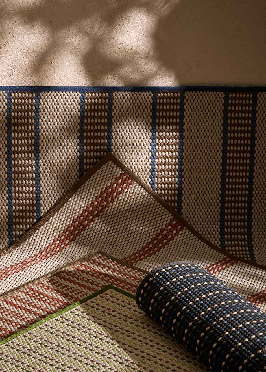 Alfombra fabricada en PET a partir de botellas de plástico recicladas de color beige con detalles en teja y elaborada en telar wilton de tejido plano.