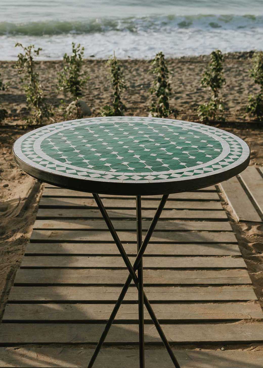 Mesa alta de exterior circular con estructura de tres pies cruzados de hierro acabado en negro.