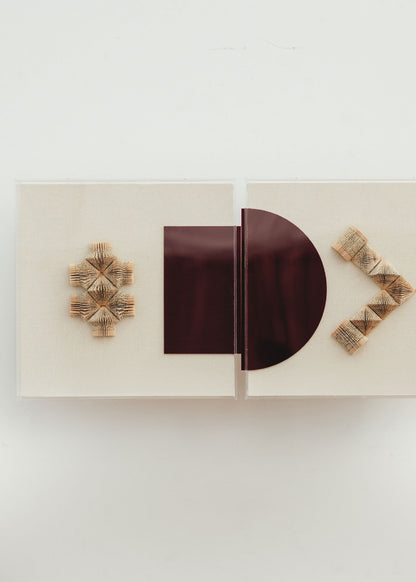 Escultura de pared forrada en lino rústico con caja de metacrilato transparente. Está formada por una serie de libros plegados y formas geométricas en metacrilato