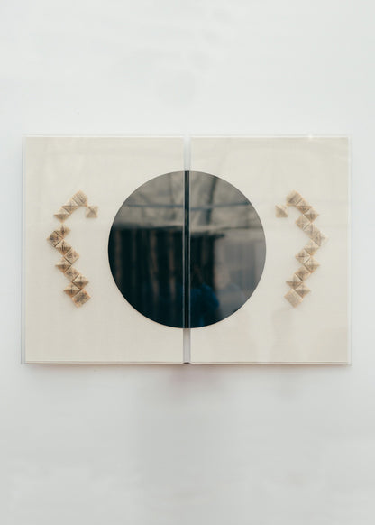 Escultura de pared en dos piezas forradas en lino rústico con cajas de metacrilato transparente. Está formada por una serie de libros plegados y formas geométricas en metacrilato.