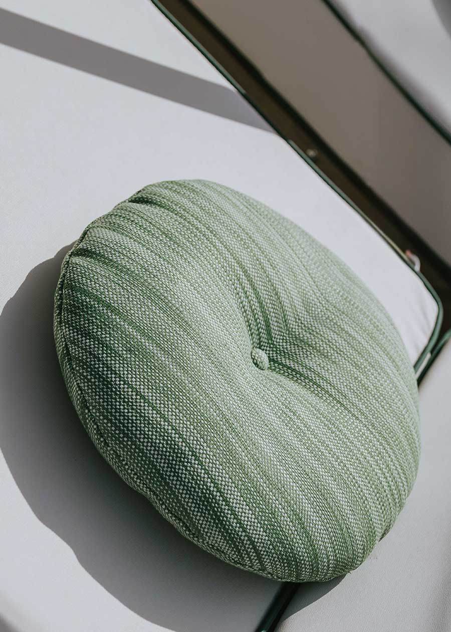 Almohadón circular con capitoné, tapizado en tela verde jaspeada.