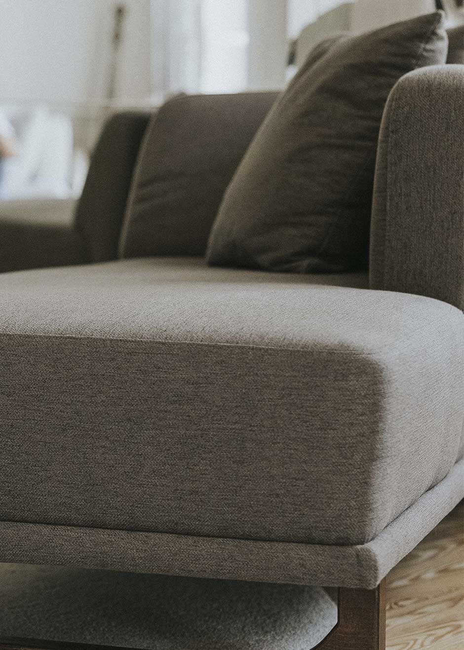 Diván con estructura y patas de madera tapizado con tela gris. 