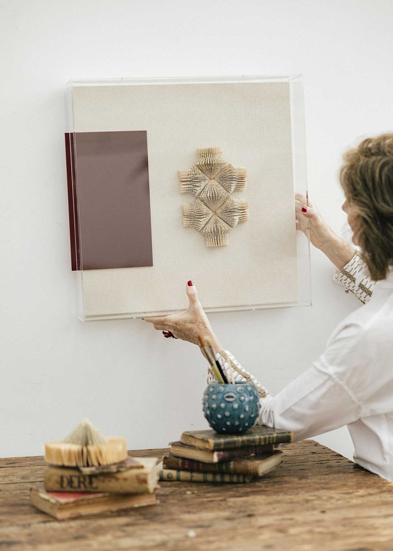 Escultura de pared forrada en lino rústico con caja de metacrilato transparente. Está formada por una serie de libros plegados y formas geométricas en metacrilato.