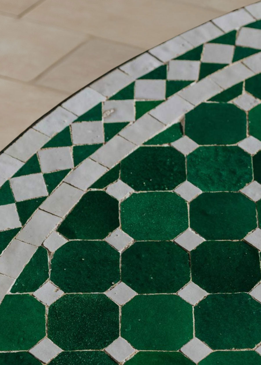 Mesa de exterior circular con estructura de hierro forjado acabado en negro y sobre en mosaico de azulejos.