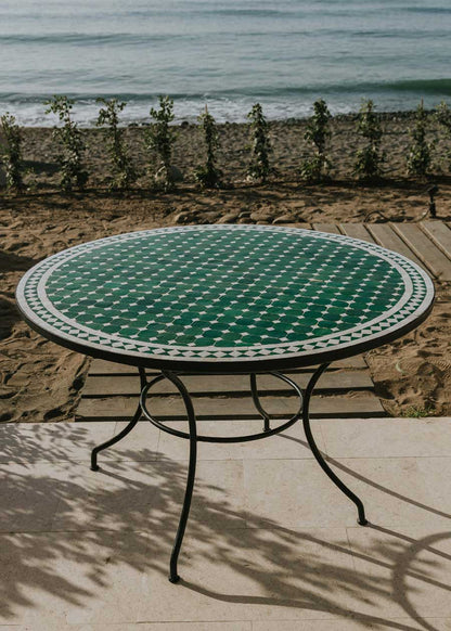Mesa de exterior circular con estructura de hierro forjado acabado en negro y sobre en mosaico de azulejos.