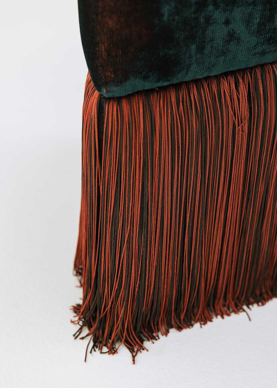 Puf triangular tapizado en terciopelo azul con detalle de flecos en la parte inferior.