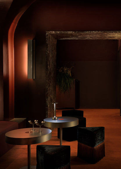 Puf triangular tapizado en terciopelo azul con detalle de flecos en la parte inferior.