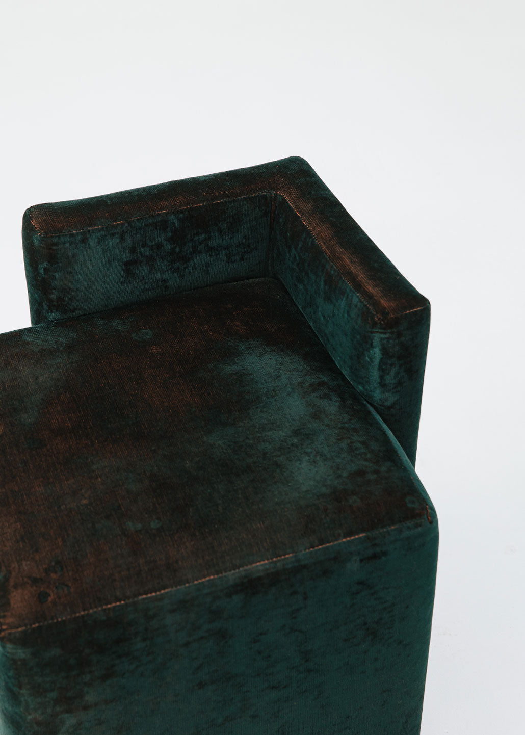 Puf cuadrado tapizado en terciopelo azul con detalle de flecos en la parte inferior.