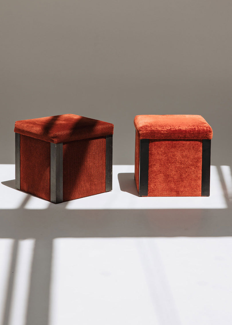 Puf cuadrado tapizado en terciopelo rojo con remates laterales de acero inoxidable.