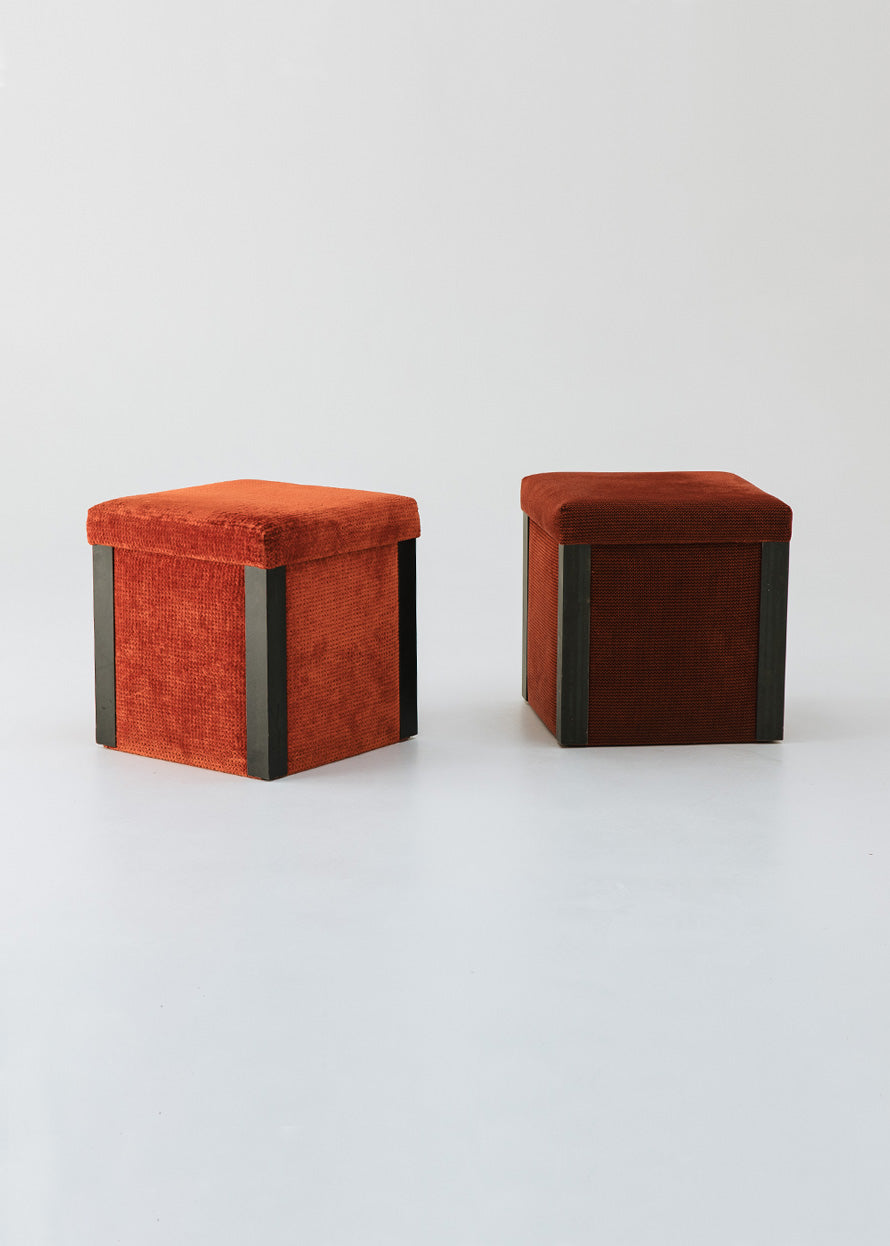 Puf cuadrado tapizado en terciopelo rojo con remates laterales de acero inoxidable.