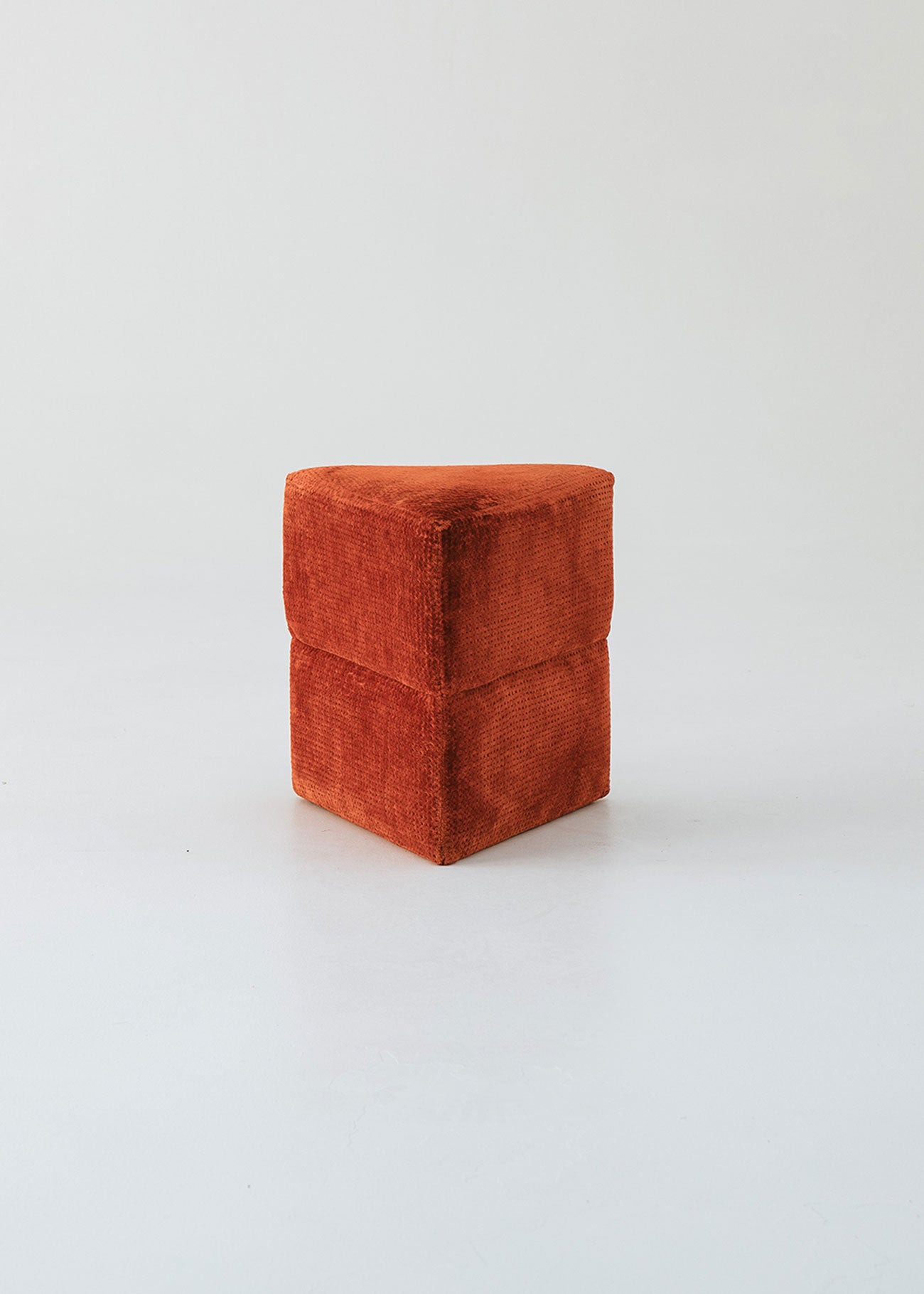 Puf triangular tapizado en tejido en tonos rojos, morados y burdeos.