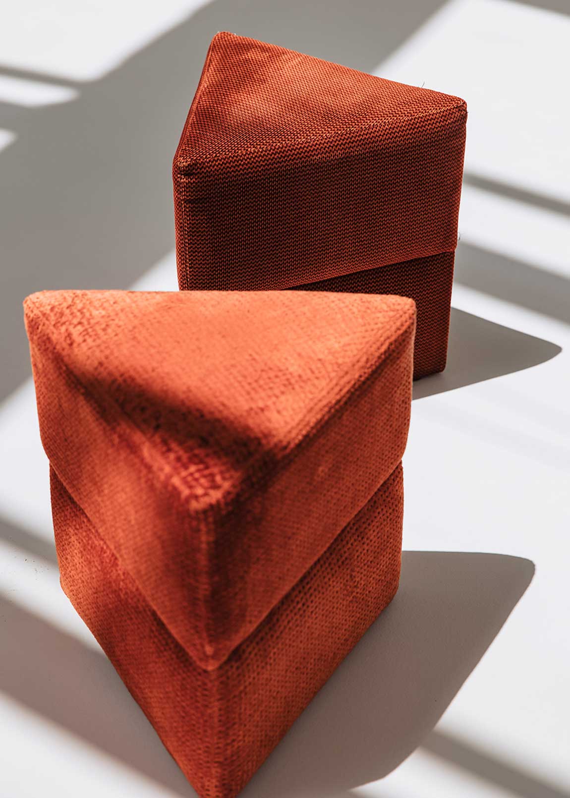 Puf triangular tapizado en tejido en tonos rojos, morados y burdeos.