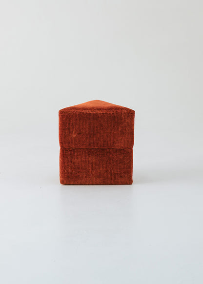 Puf triangular tapizado en tejido en tonos rojos, morados y burdeos.