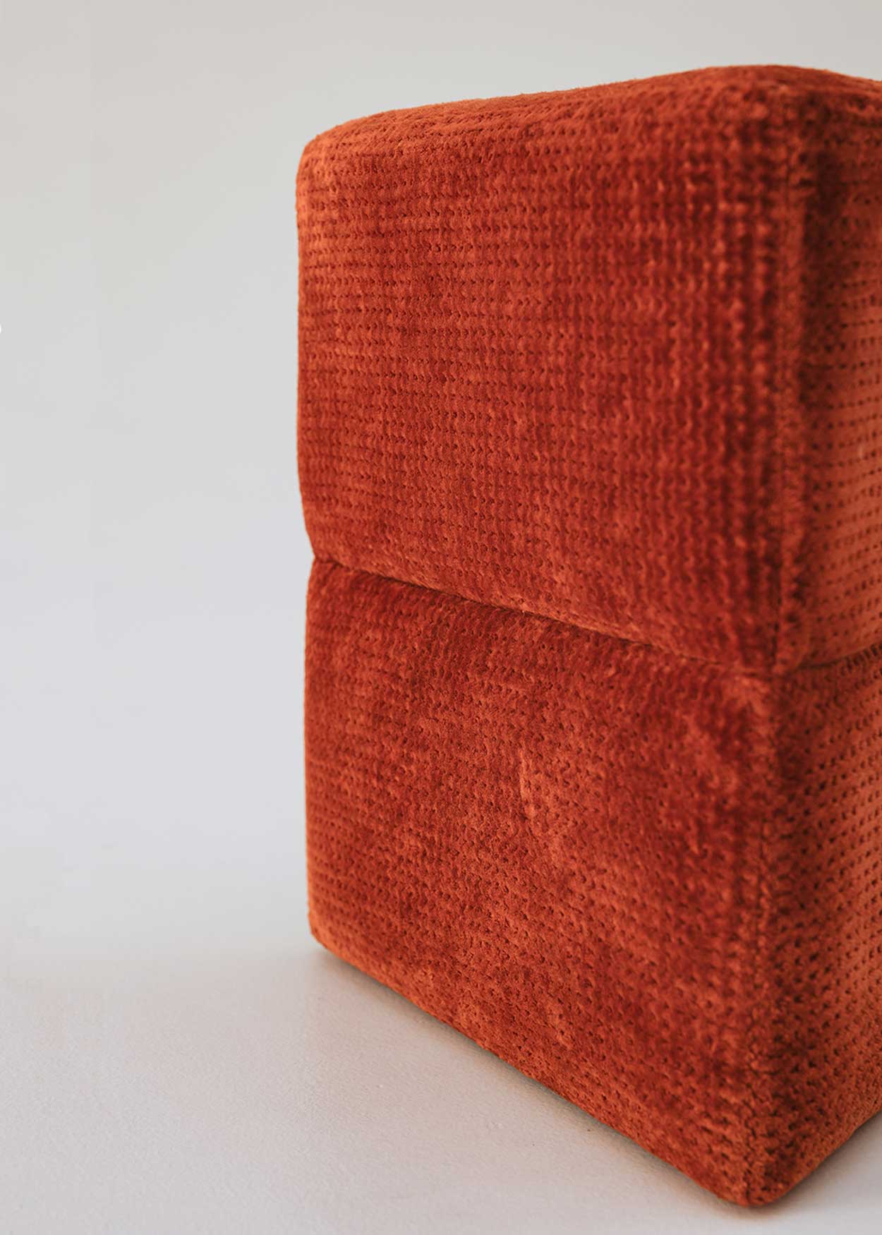 Puf triangular tapizado en tejido en tonos rojos, morados y burdeos.