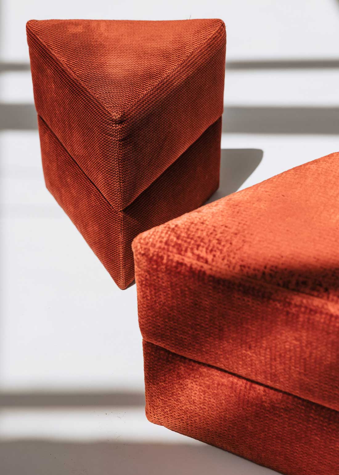 Puf triangular tapizado en tejido en tonos rojos, morados y burdeos.