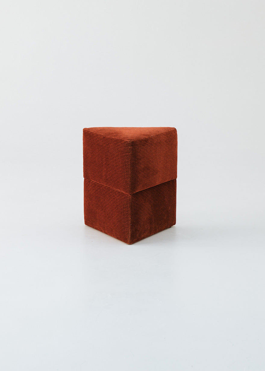 Puf triangular tapizado en tejido en tonos rojos, morados y burdeos.