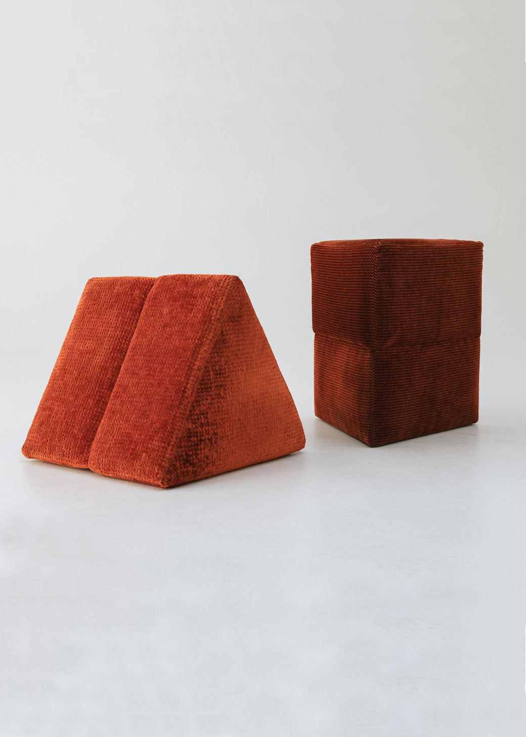 Puf triangular tapizado en tejido en tonos rojos, morados y burdeos.