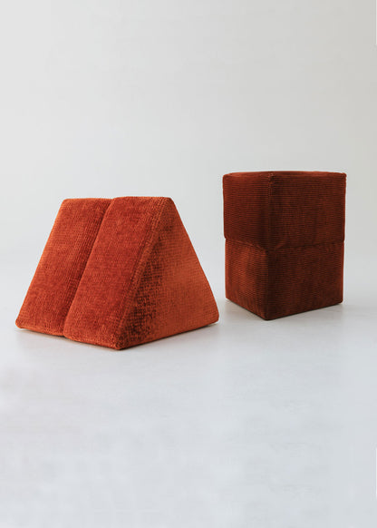 Puf triangular tapizado en tejido en tonos rojos, morados y burdeos.