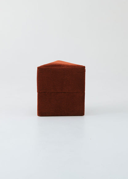 Puf triangular tapizado en tejido en tonos rojos, morados y burdeos.