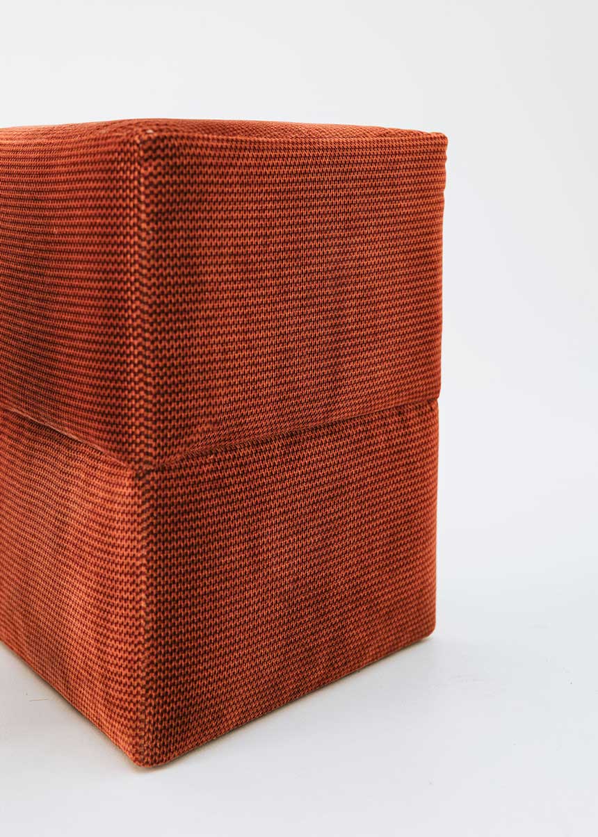 Puf triangular tapizado en tejido en tonos rojos, morados y burdeos.