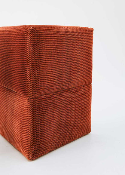 Puf triangular tapizado en tejido en tonos rojos, morados y burdeos.