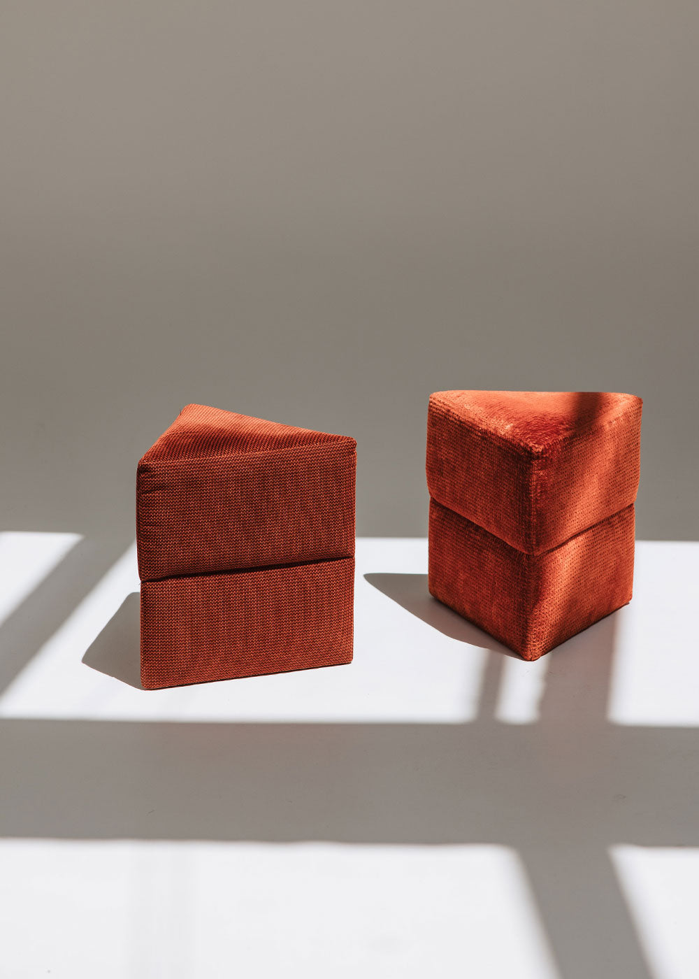 Puf triangular tapizado en tejido en tonos rojos, morados y burdeos.