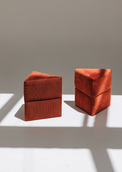 Puf triangular tapizado en tejido en tonos rojos, morados y burdeos.