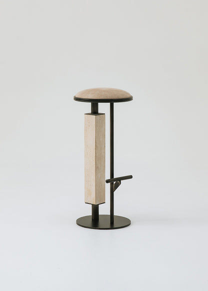 Taburete tapizado con estructura de hierro con detalle de piedra travertino. Un taburete alto con reposapiés y asiento tapizado en tela de terciopelo beige.