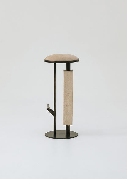 Taburete tapizado con estructura de hierro con detalle de piedra travertino. Un taburete alto con reposapiés y asiento tapizado en tela de terciopelo beige.