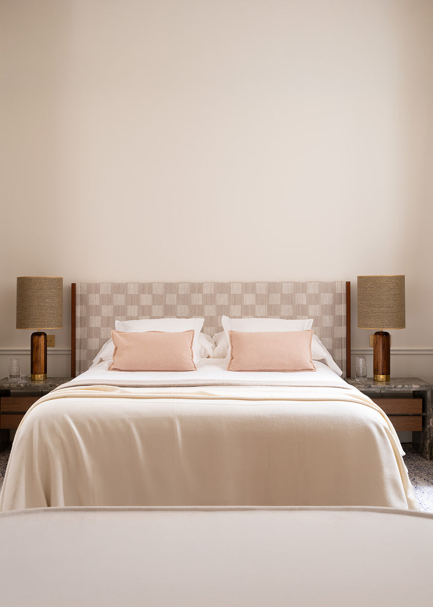 Cabecero tapizado en tela damero con laterales de madera de nogal vista.