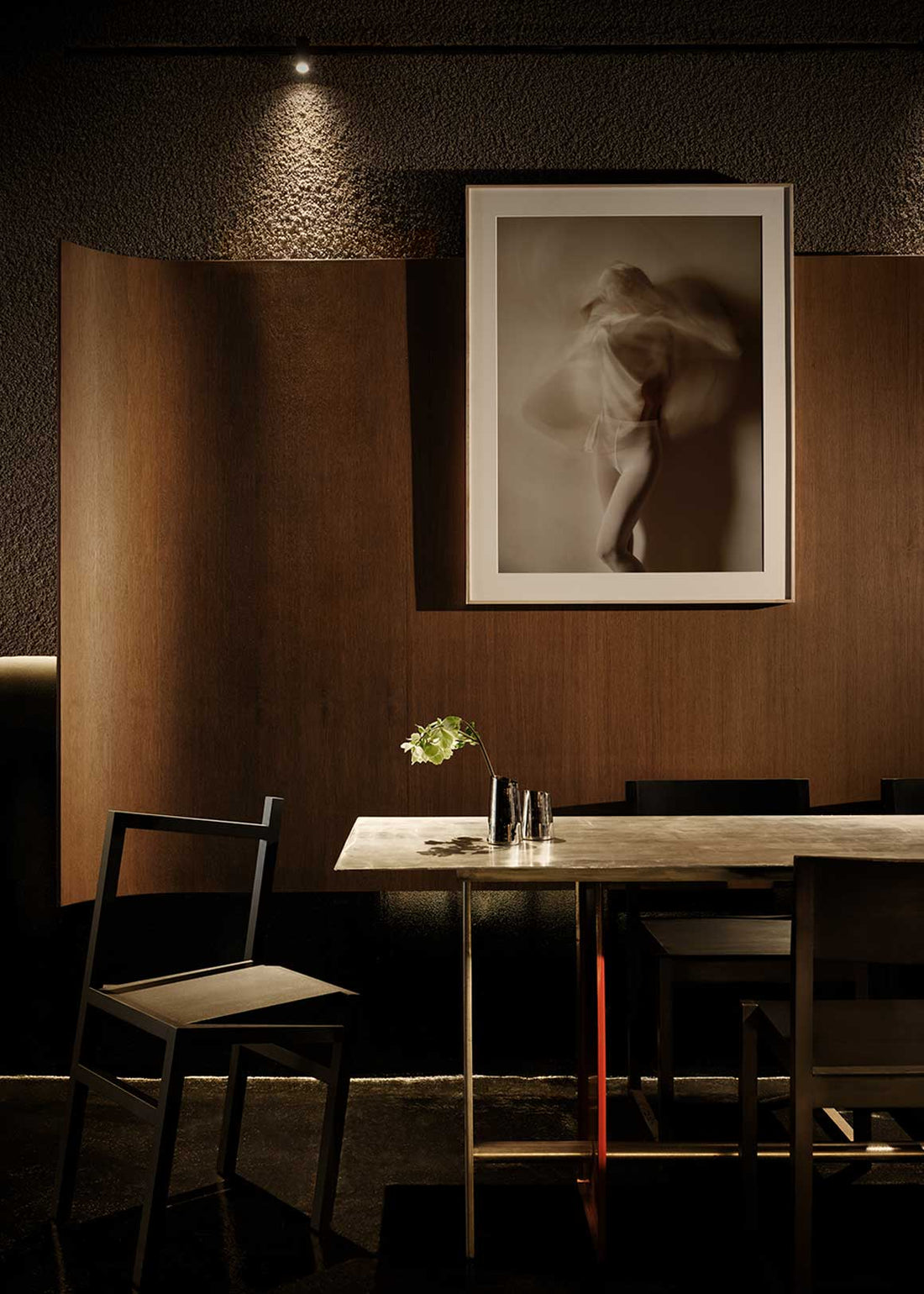 Mesa de comedor rectangular con estructura metálica de acero inoxidable cepillado para patas y sobre. Una de las patas va lacada en rojo.