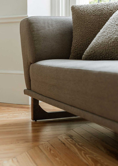 Diván con estructura y patas de madera tapizado con tela gris. Incluye almohadones con relleno en fibra.