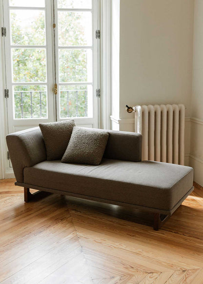 Diván con estructura y patas de madera tapizado con tela gris. Incluye almohadones con relleno en fibra.