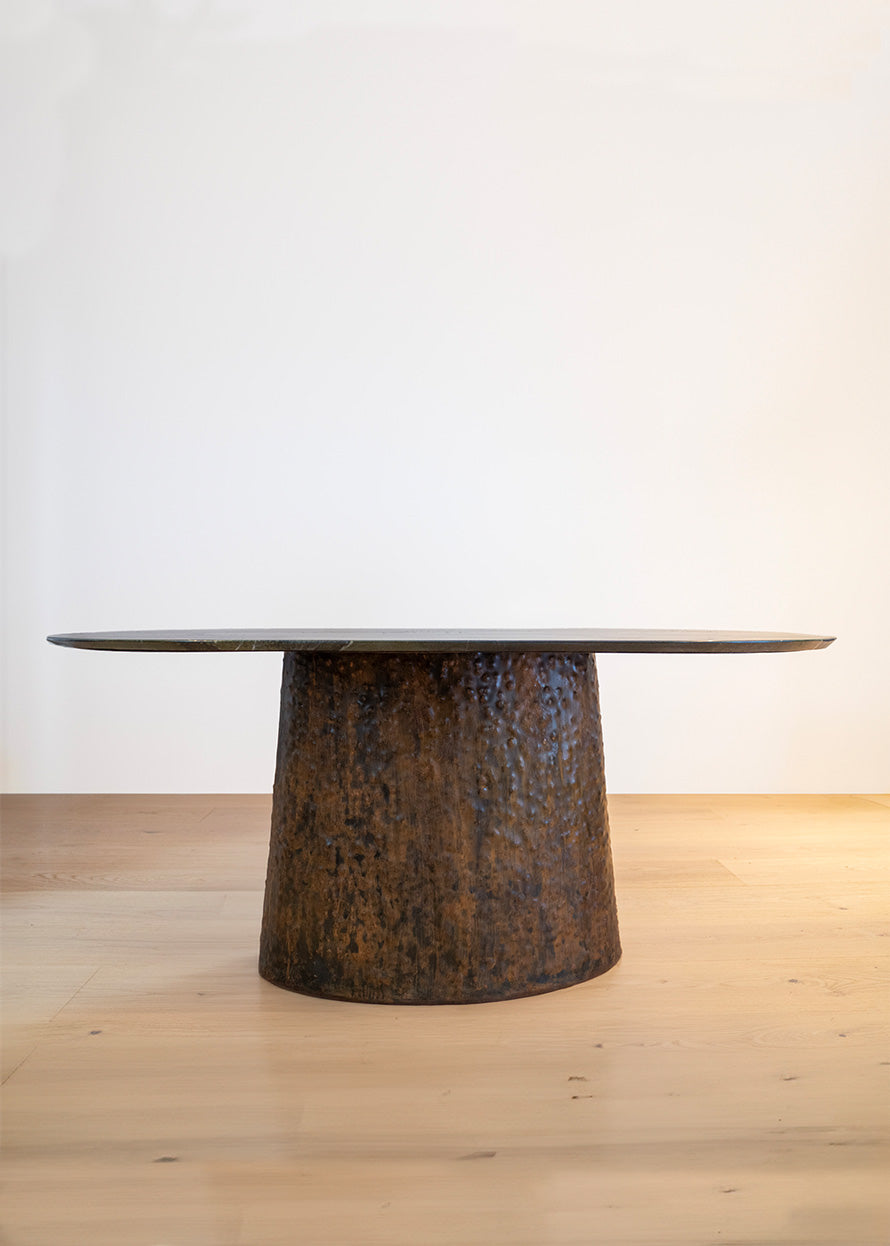 Mesa de comedor de cuarcita Avocatus con borde en pico de flauta y pie de metal oxidado con acabado martilleado y capa protectora.