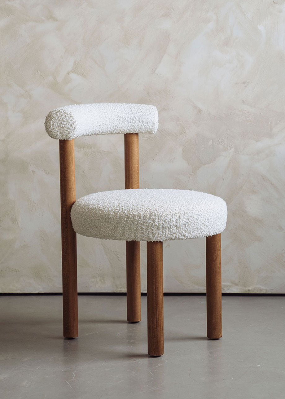 Silla de madera de haya tapizada en bouclé blanco con respaldo semicircular.