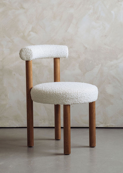 Silla de madera de haya tapizada en bouclé blanco con respaldo semicircular.