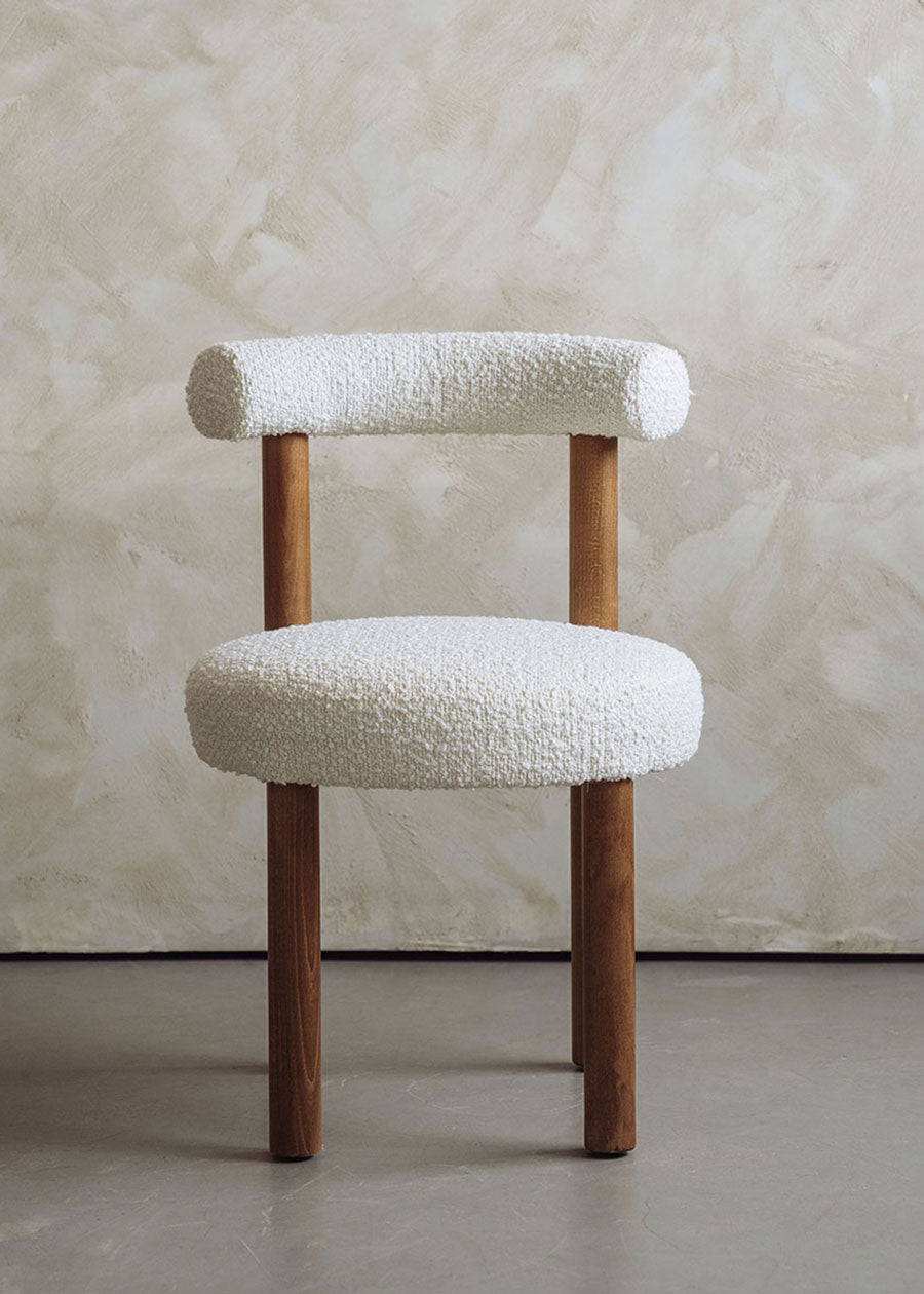 Silla de madera de haya tapizada en bouclé blanco con respaldo semicircular.
