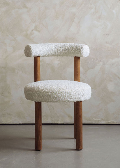 Silla de madera de haya tapizada en bouclé blanco con respaldo semicircular.