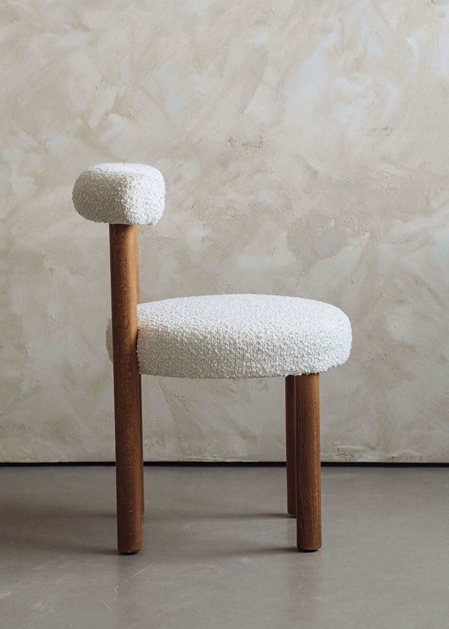Silla de madera de haya tapizada en bouclé blanco con respaldo semicircular.