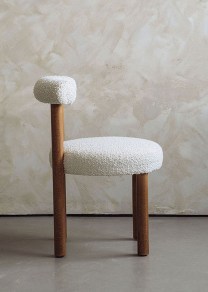 Silla de madera de haya tapizada en bouclé blanco con respaldo semicircular.