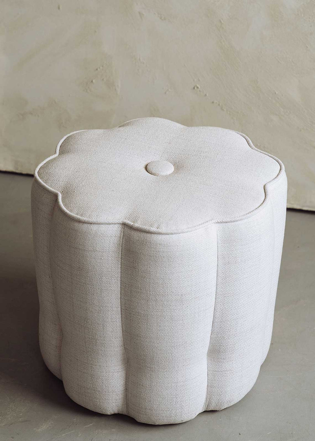 Otomana con forma de flor tapizada en tela blanca.