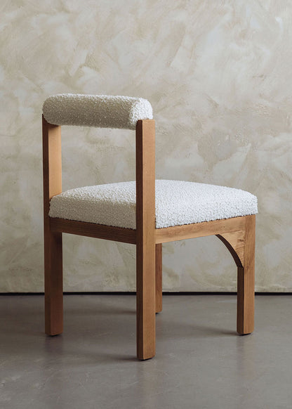 Silla de madera de haya tapizada en bouclé blanco con respaldo cilíndrico.