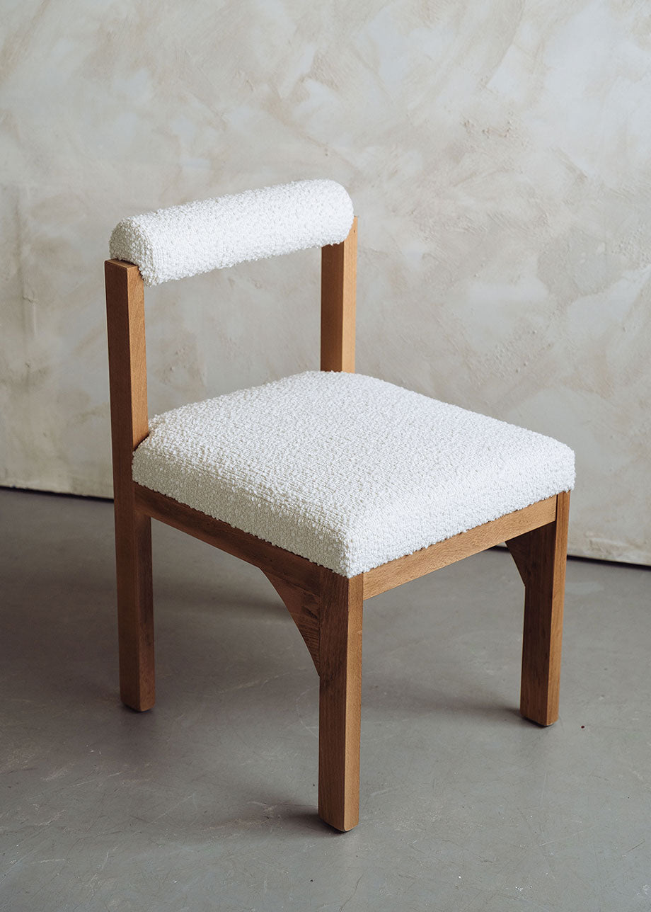 Silla de madera de haya tapizada en bouclé blanco con respaldo cilíndrico.
