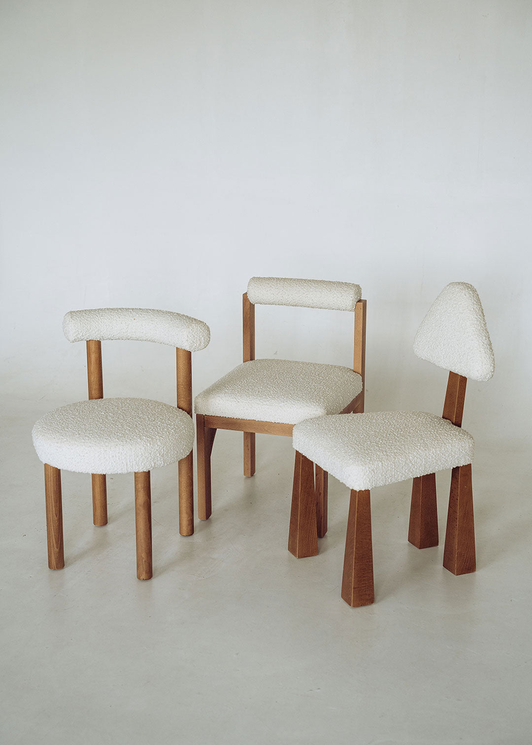 Silla de madera de haya tapizada en bouclé blanco con respaldo triangular.