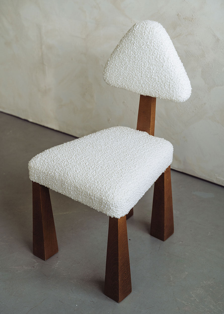 Silla de madera de haya tapizada en bouclé blanco con respaldo triangular.