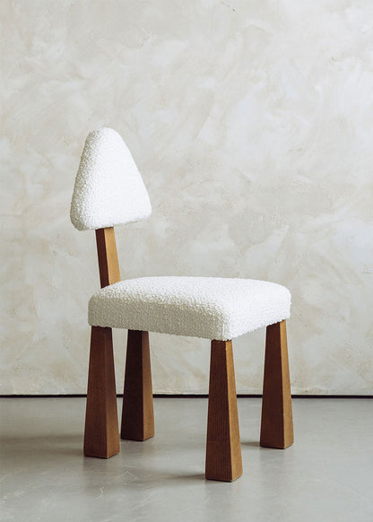 Silla de madera de haya tapizada en bouclé blanco con respaldo triangular.