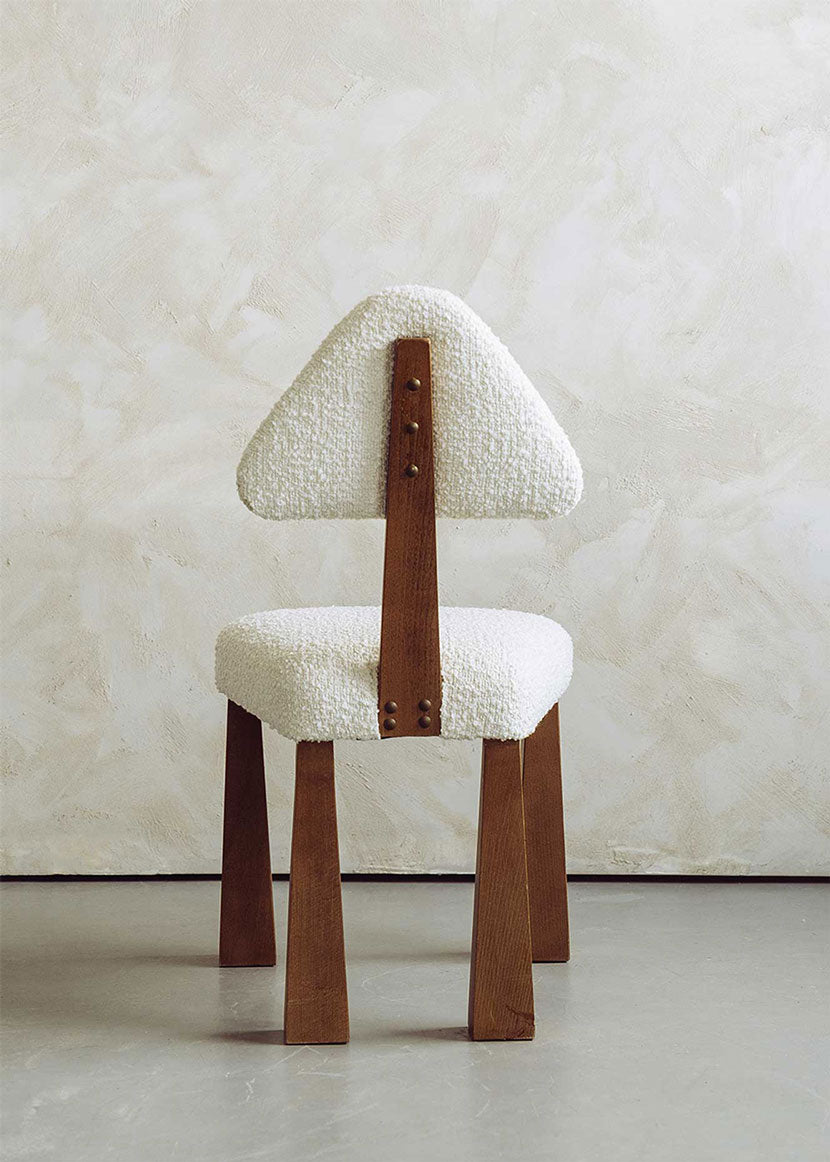 Silla de madera de haya tapizada en bouclé blanco con respaldo triangular.